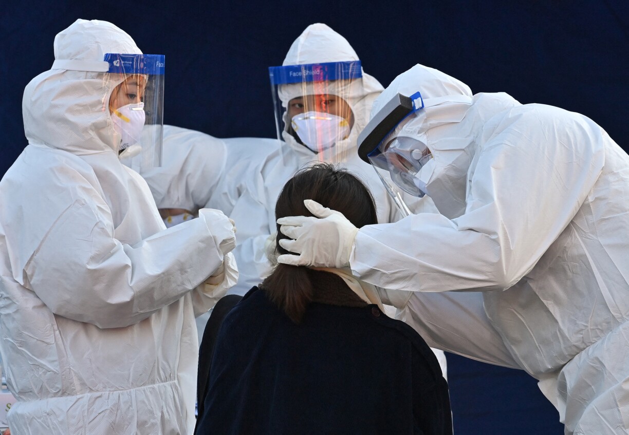 A medical staff member wearing protective gear takes a swab from a woman to test for the Covid-19 coronavirus at a temporary testing station outside Seoul station in Seoul on December 14, 2020.