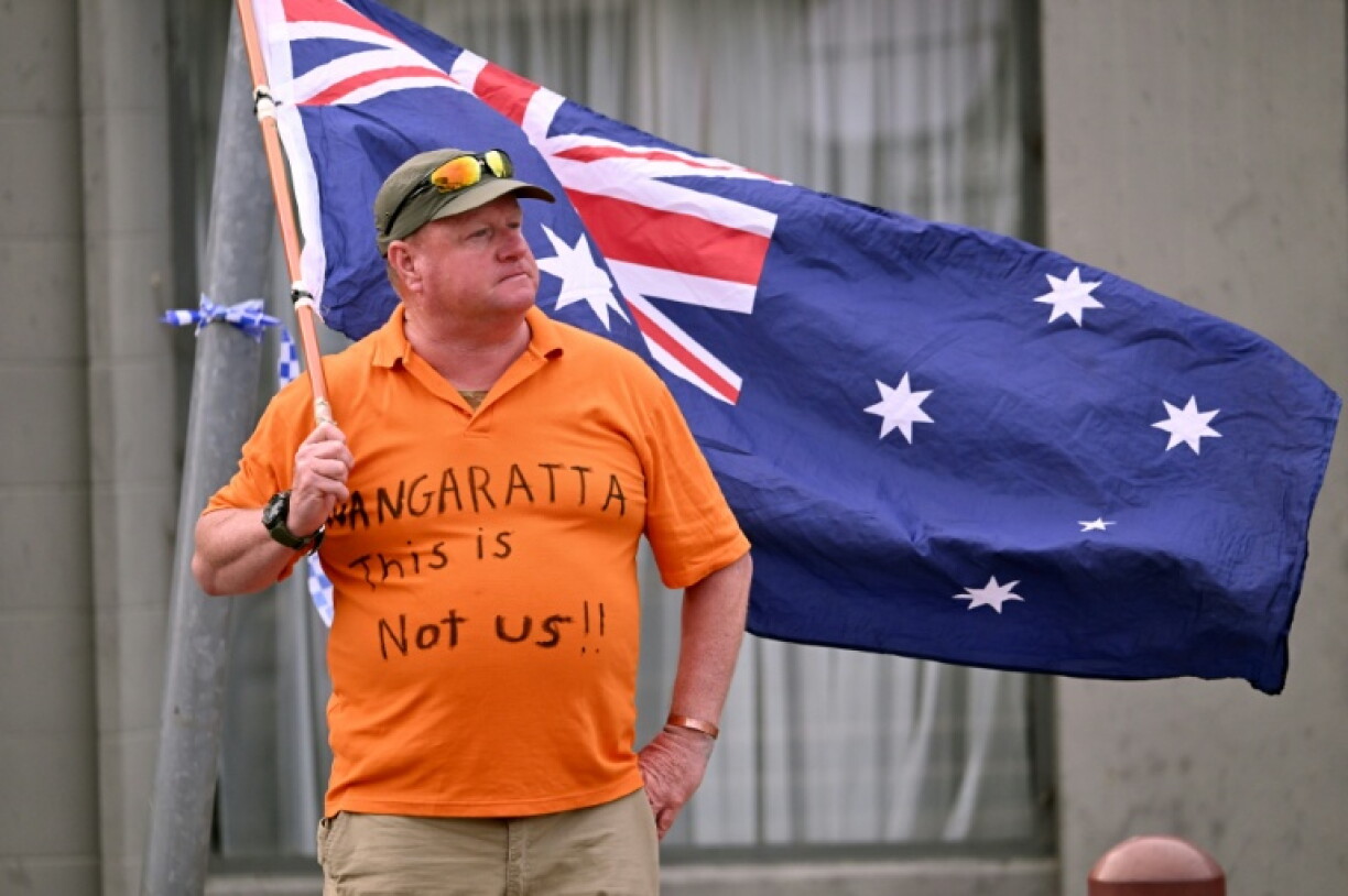 A man holds an Australian flag outside the office of Australian politician Helen Haines in the northern regional city of Wangaratta, about 250 kilometres north-east of Melbourne on October 20, 2026. Australian independent lawmaker Helen Haines underwent surgery overnight but remains in a critical condition after being struck deliberately by a car in an attack, Prime Minister Anthony Albanese said on October 20. Political violence is rare in Australia, but law enforcement have documented a steady rise in threats and abuse directed towards the nation's elected officials in recent years.