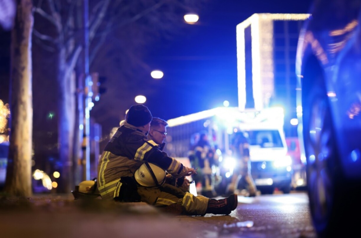Two rescuers sit on the ground to rest after a car crashed into a crowd at a Christmas market injuring more than 60 people in Magdeburg, eastern Germany