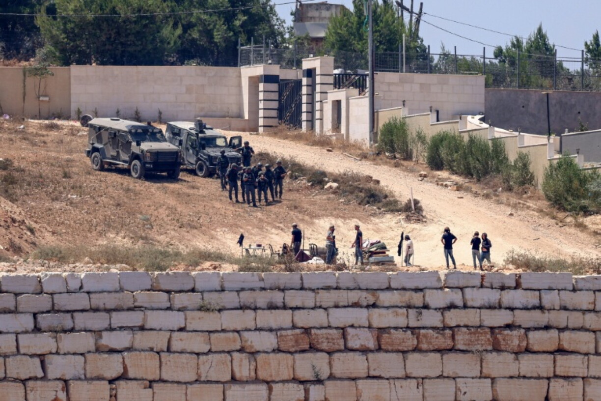 Des soldats israéliens face à des colons assiégeant des maissons palestiniennes du village de Qusra, en Cisjordanie occupée, le 12 août 2026