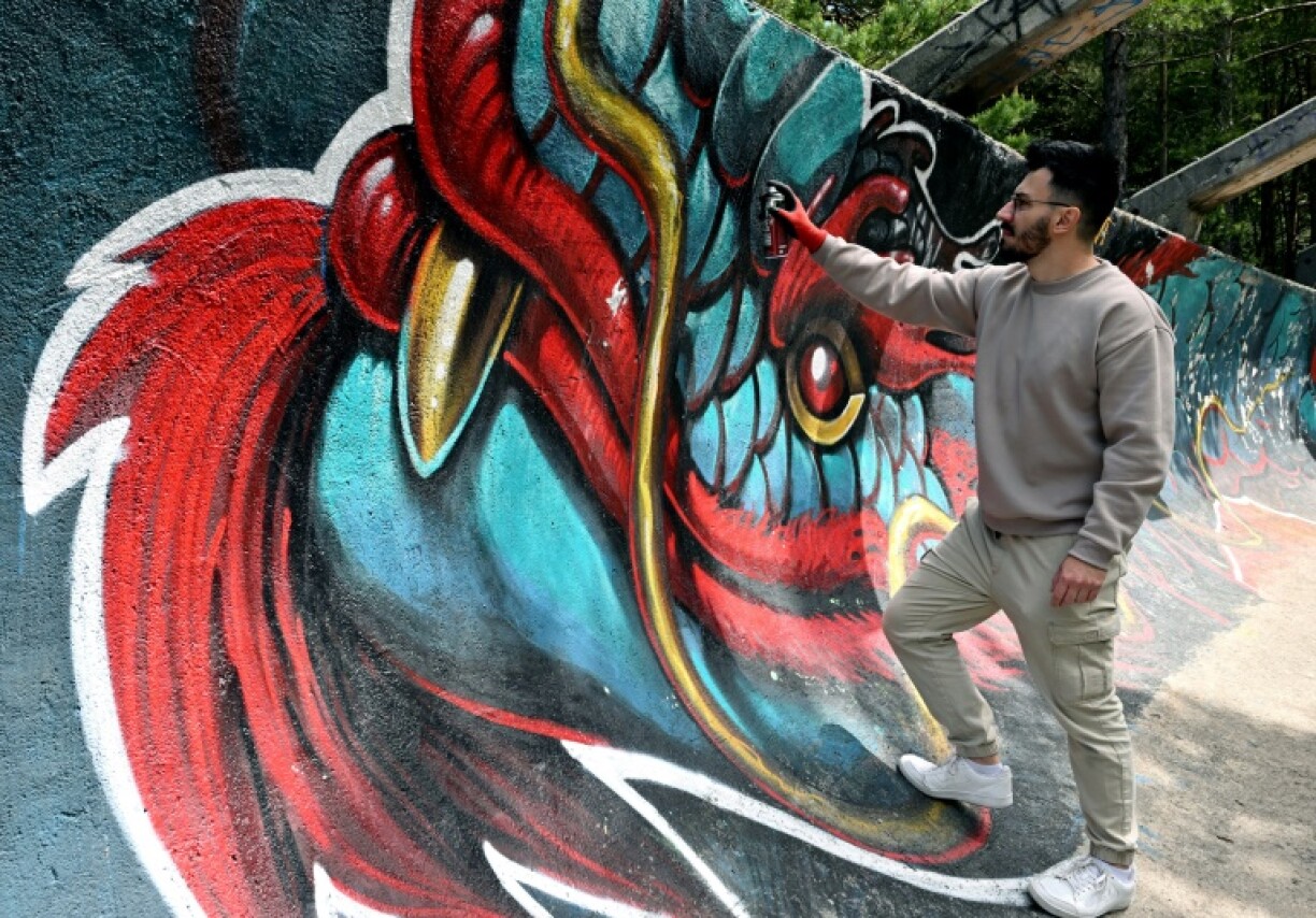 Street artist Kerim Musanovic puts the finishing touches to touches to a painting on the former Olympic bobsled track at Mount Trebevic, near Sarajevo