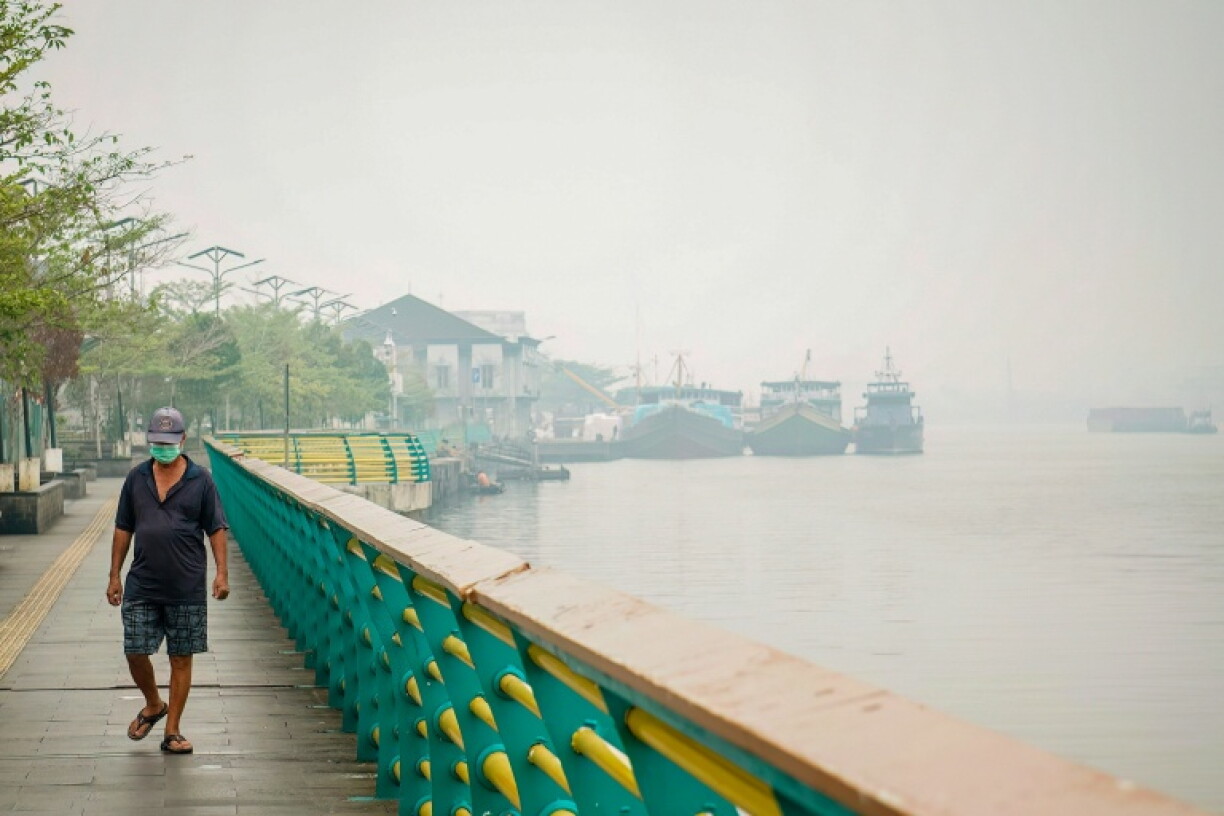 Un homme portant un masque marche le long d’une berge tandis qu’un brouillard dû aux feux de forêt et de végétation enveloppe le village de Benua Melayu Laut, à Pontianak,à Bornéo en Indonésie, le 17 septembre 2026