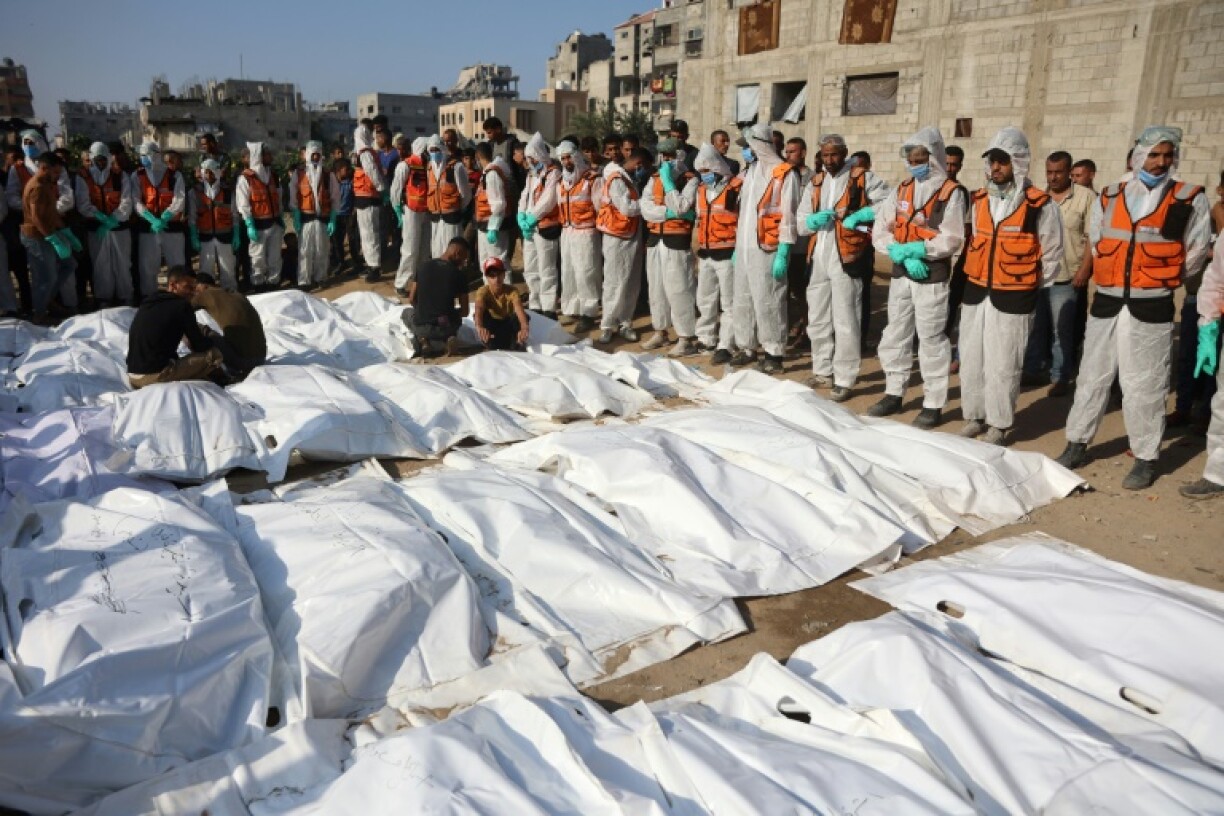 Civil Defense members stand by after laying out body bags containing the remains of members of the Shahebar family, who were buried in temporary graves, as they are brought to a cemetery in Gaza City
