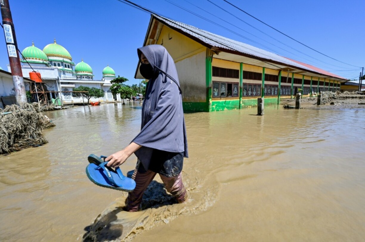 Une habitante marche près d'une mosquée dans zone inondée, le 30 novembre 2025 à Meureudu en Indonésie