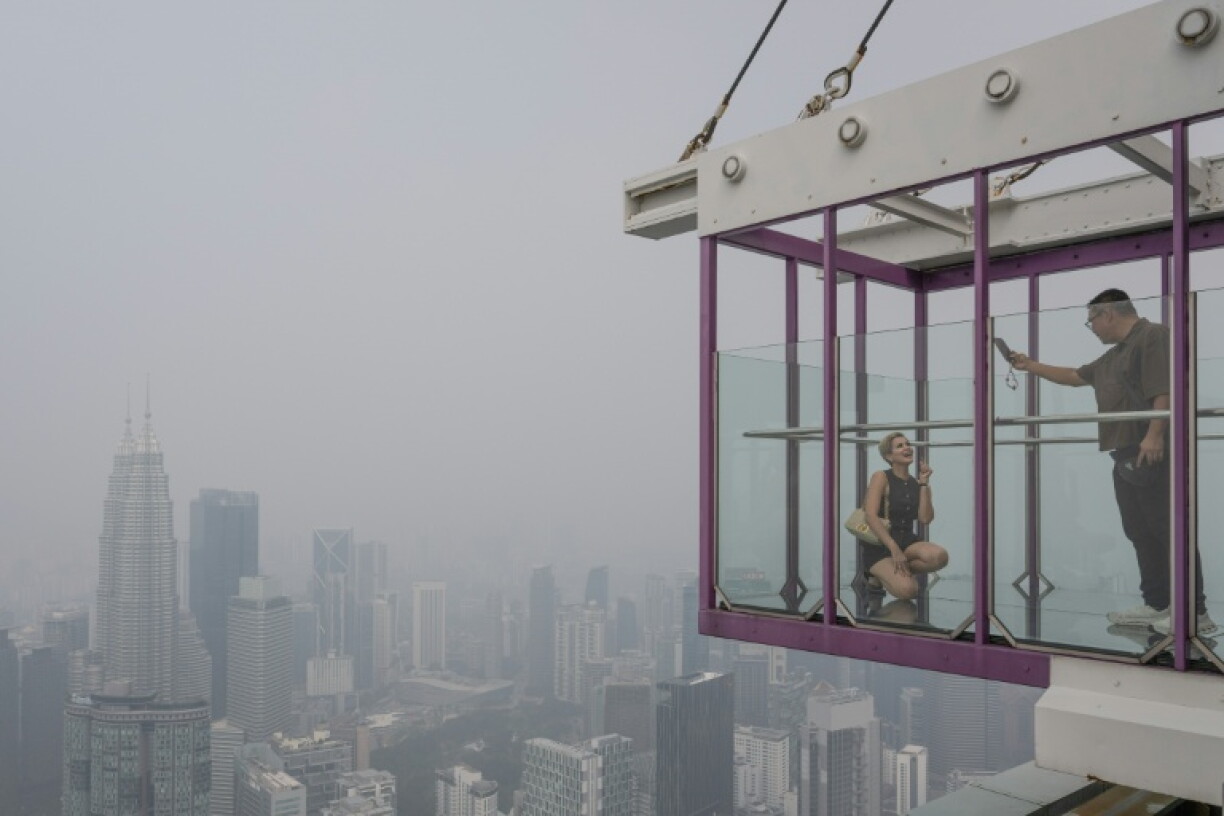 A tourist takes pictures with Malaysia’s Petronas Twin Towers and commercial buildings covered by haze in Kuala Lumpur