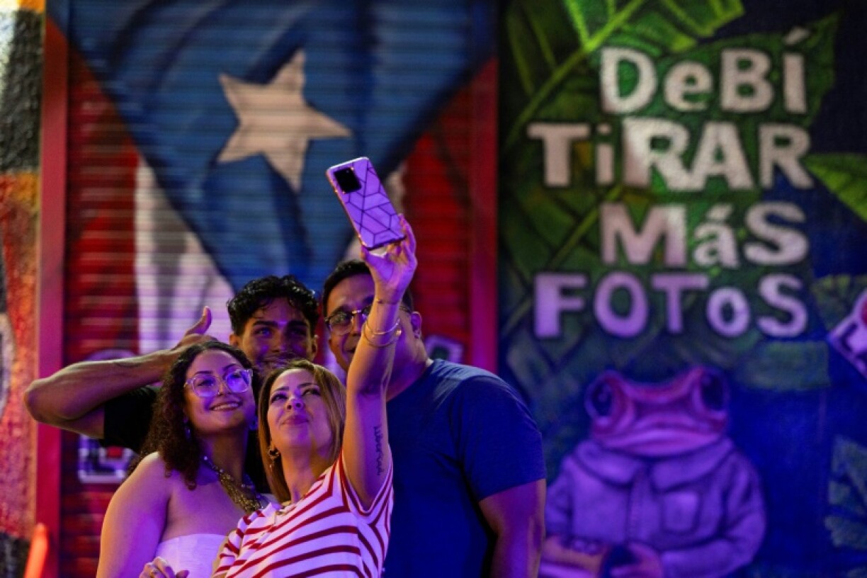 A group of people take a selfie in front of a mural at La Placita de Santurce in San Juan, Puerto Rico on May 12, 2025