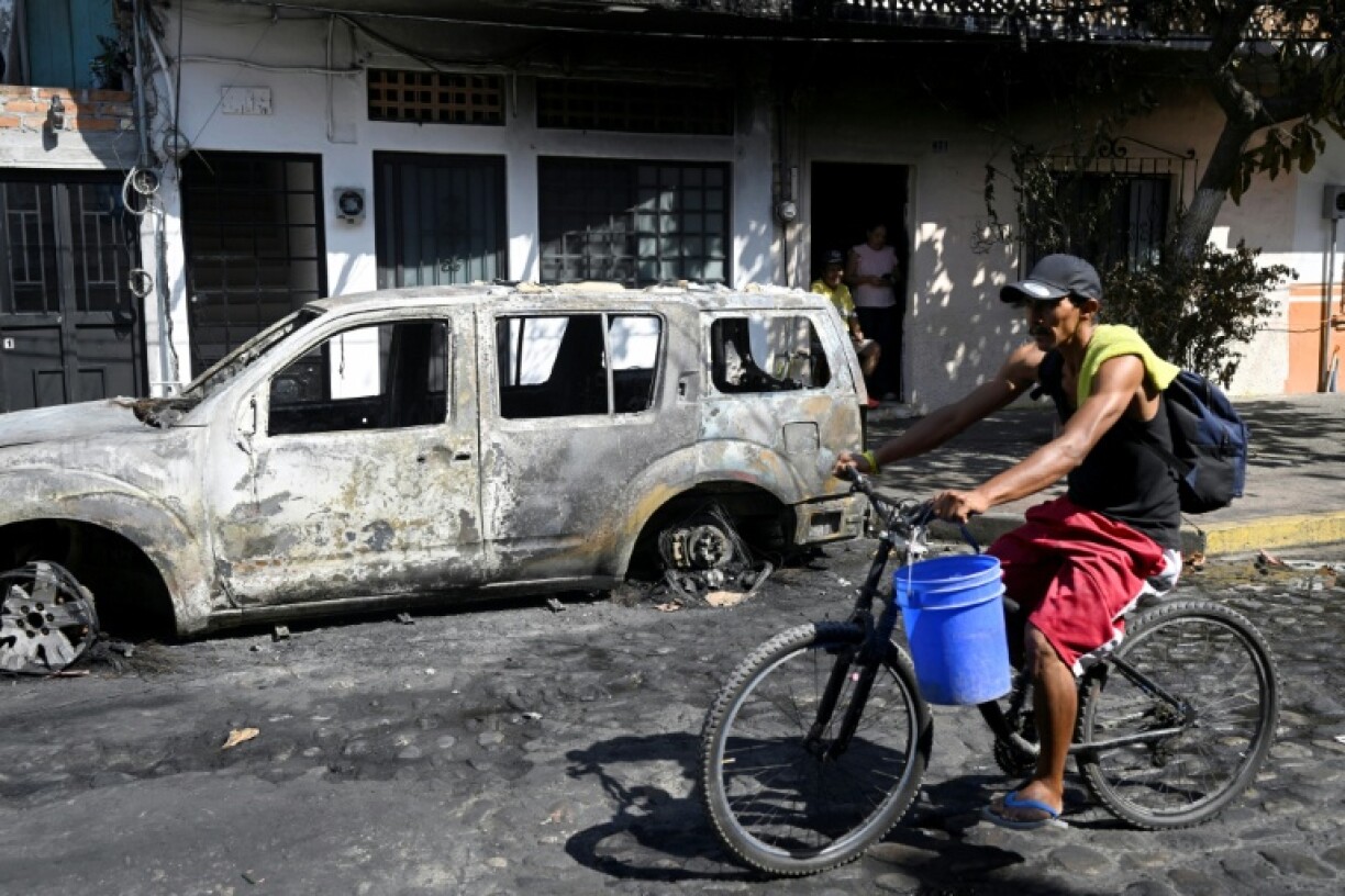 Un homme passe à vélo devant un véhicule incendié à Puerto Vallarta, dans l'Etat de Jalisco, au Mexique, le 24 février 2026