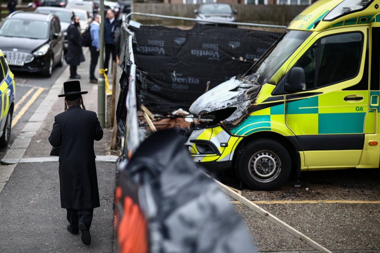 A member (L) of the Jewish community walks past the scene of an antisemitic arson attack in the Golders Green neighbourhood of north London, on 24 March 2026, a day after volunteer ambulances run by a Jewish organisation were set on fire.
