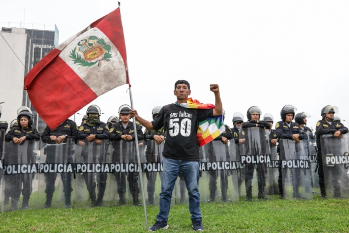 A demonstrator holds a Peruvian flag and wears a shirt that reads