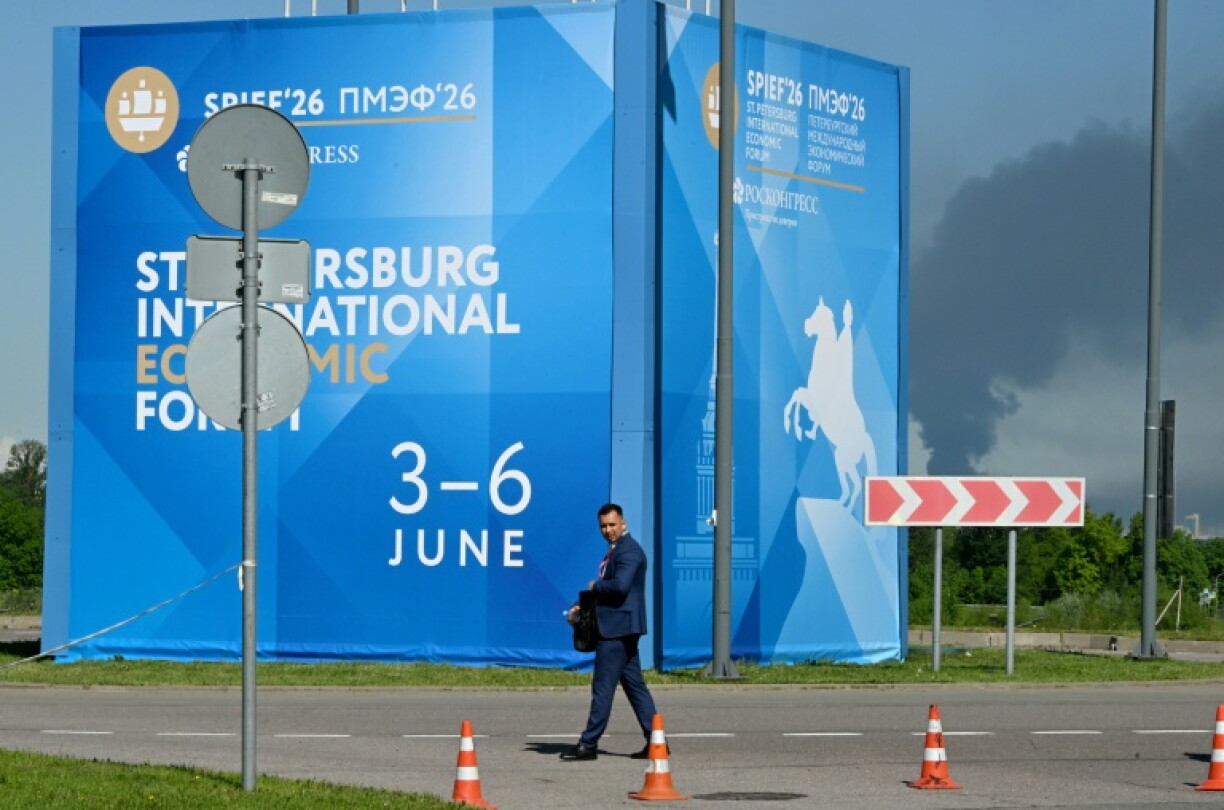 Un homme passe devant des affiches du Forum économique international de Saint-Pétersbourg alors que de la fumée s'élève en arrière-plan après des frappes de drones ukrainiens, le 3 juin 2026 en Russie