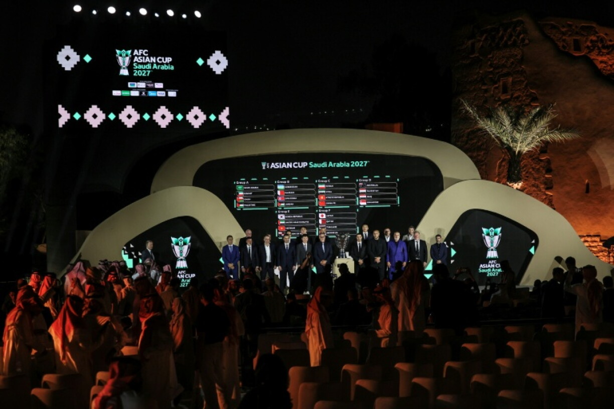Coaches of Asian national football teams pose in front of a screen showing the results of the draw last year