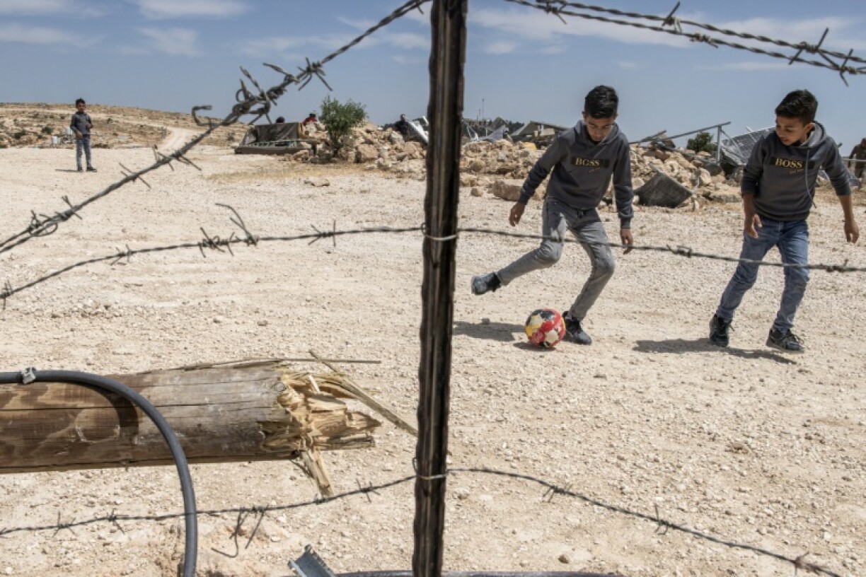 Children play football in front of the rubble of a demolished house