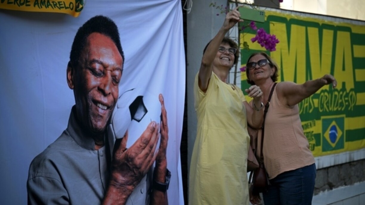 Des personnes en deuil prennent un selfie à côté de l'image du joueur de football brésilien Pelé, devant le stade Urbano Caldeira, dans l'État de Sao Paulo, au Brésil, le 2 janvier 2023