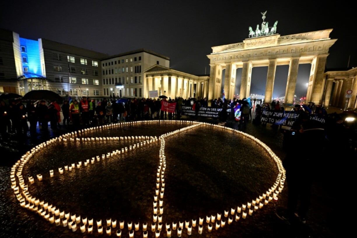 Des dizaines de bougies forment le symbole de la paix, au pied de la porte de Brandebourg, le 23 février 2023 à Berlin