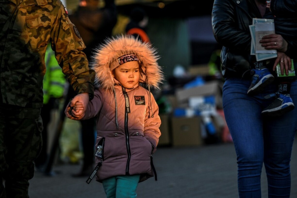 Soldat polonais tenant la main d'une fillette réfugiée qui vient de passer la frontière ukrainienne avec sa famille à Medyka en Pologne, le 11 mars 2022