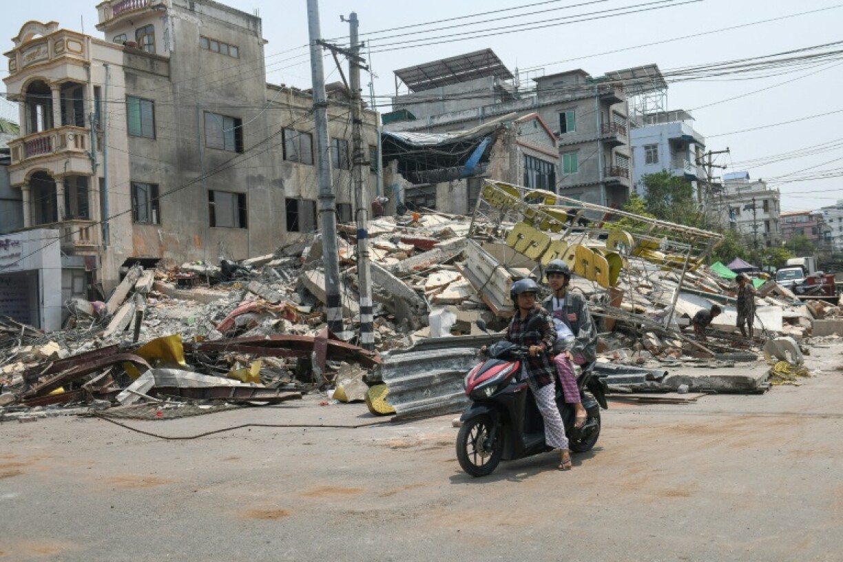 People ride a motorbike past damaged buildings in Mandalay, Myanmar