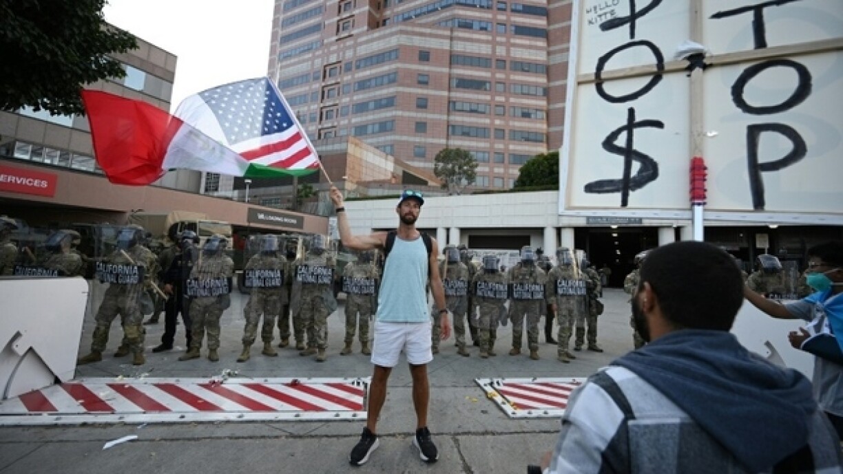 Un homme brandit un drapeau aux couleurs des Etats-Unis et du Mexique devant des membres de la Garde nationale, à Los Angeles (Californie), le 12 juin 2025