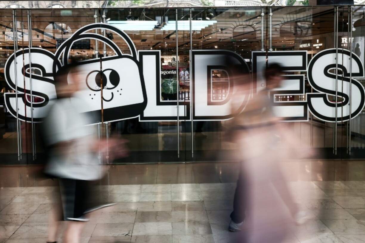 Des passants marchent à proximité de l'entrée d'un centre commercial annonçant les soldes, le 25 juin 2025 à Paris