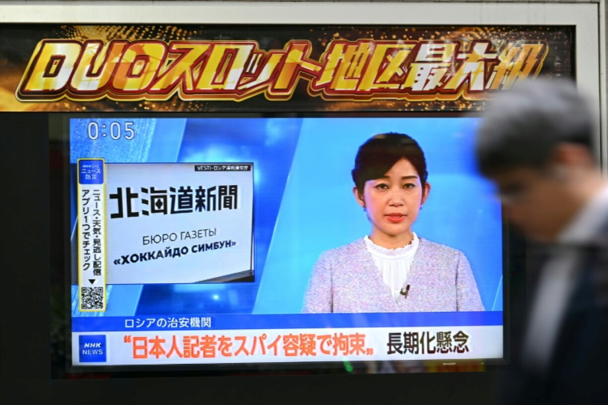 A man walks past a screen displaying a news brodcast in Tokyo on October 14, 2026, reporting on the arrest of Japanese reporter Yuki Imai, from the Hokkaido Shimbun newspaper, after he was taken into custody by Russia on suspicion of espionage on the far east island of Sakhalin.