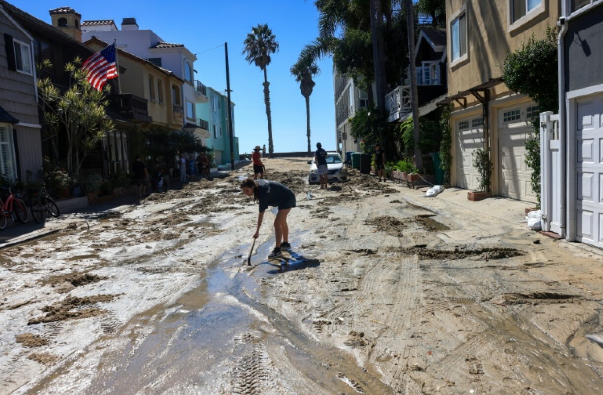 A woman shovels sand brought by the storm surge onto a street in Long Beach, California, which could see more coastal flooding into the weekend