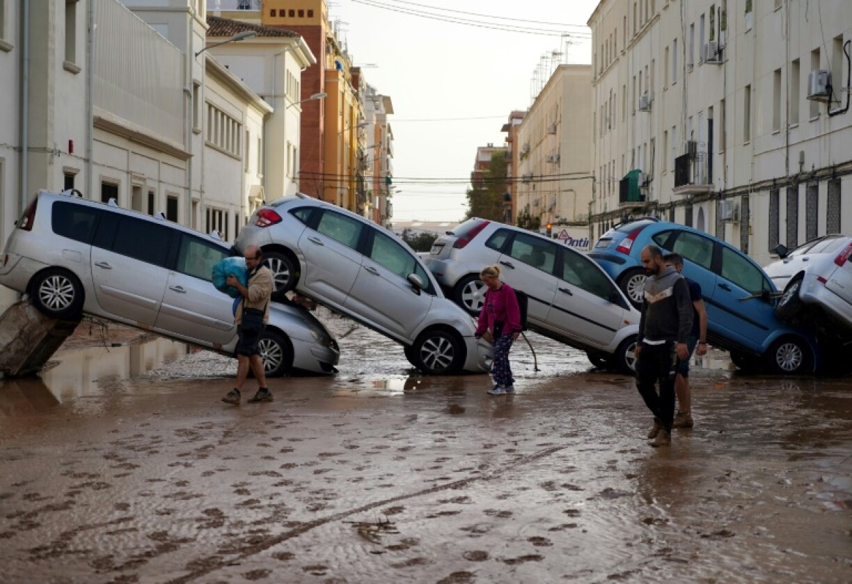 Des habitants marchent dans la boue devant des voitures empilées par les inondations à Sedavi, près de Valence, dans l'est de l'Espagne, le 30 octobre 2024.