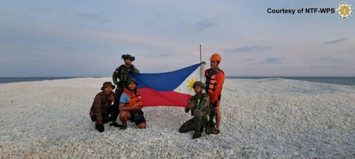 Members of the Philippine Coast Guard unfurl the national flag during a trip to a disputed reef that Chinese media had reported was under Beijing's control