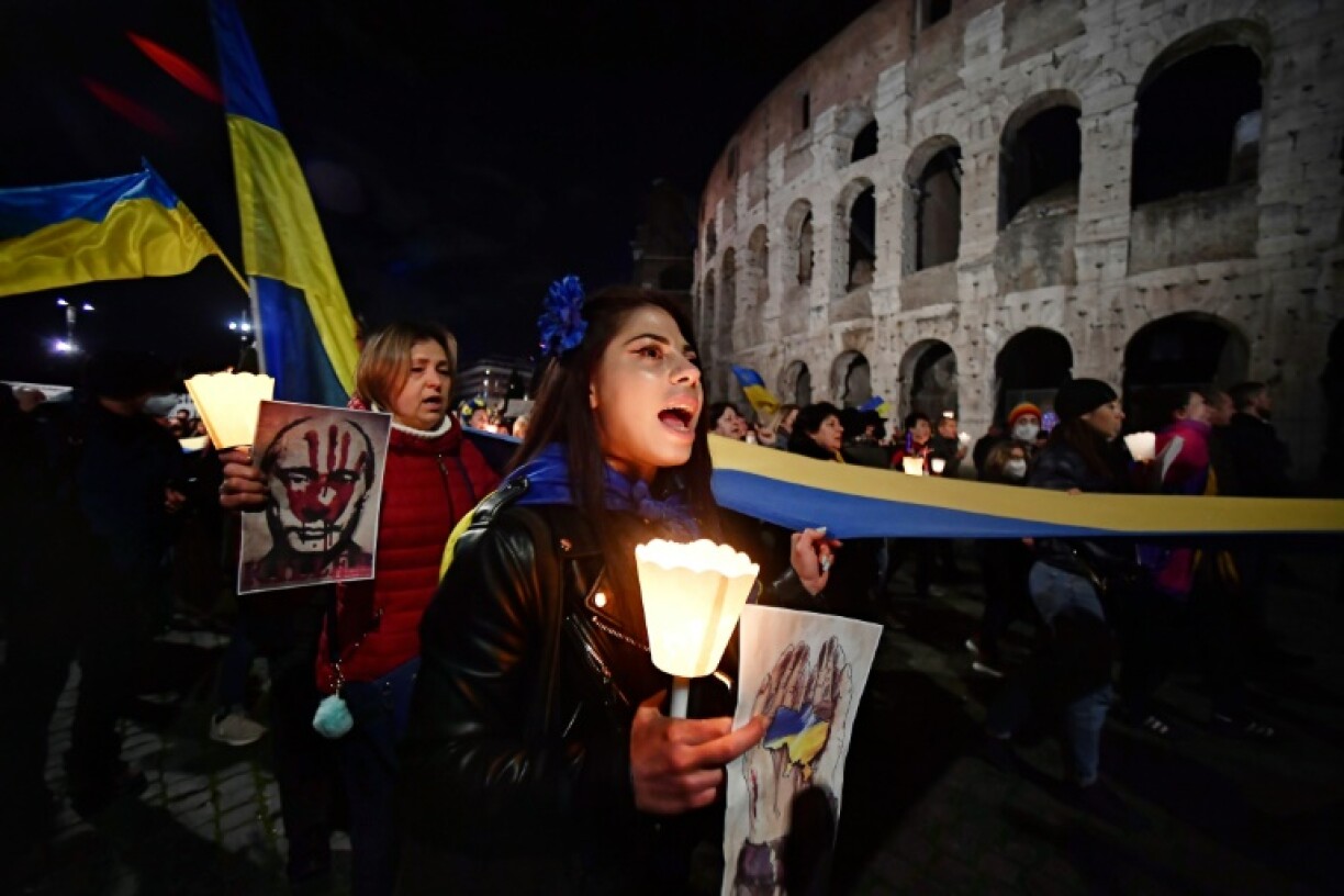 Des manifestants tiennent un drapeau national ukrainien géant et des bougies pendant un rassemblement contre l'invasion russe de l'Ukraine, à Rome le 25 février 2022