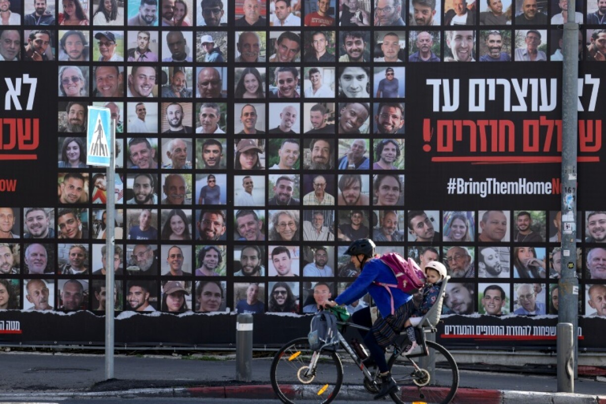 A man rides a bicycle past a billboard in Jerusalem featuring portraits of Israeli hostages held in the Gaza Strip