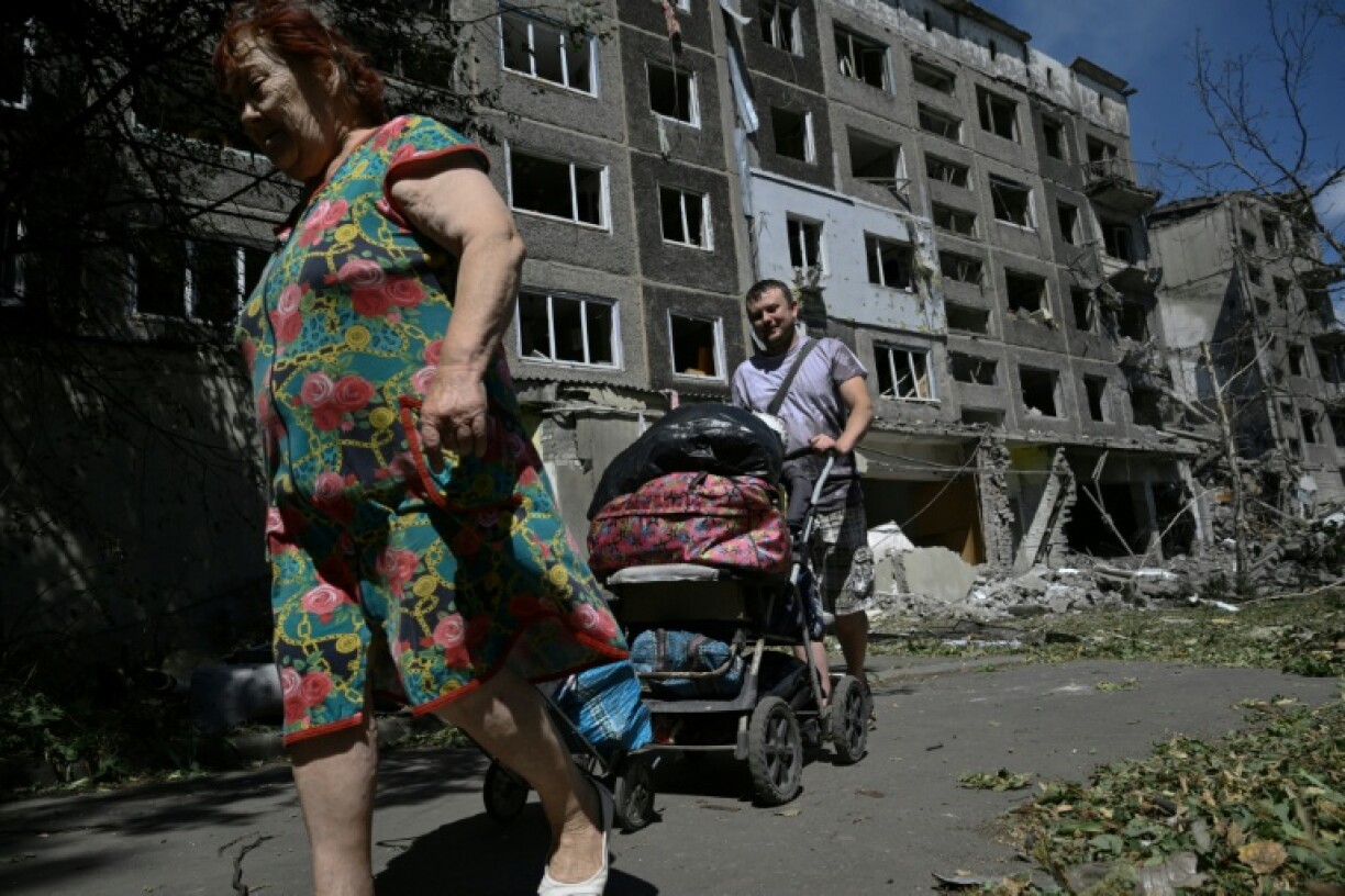 Local residents carry their belongings out of a heavily damaged residential building following a Russian strike in the town of Bilozerske, Donetsk region on August 12, 2025