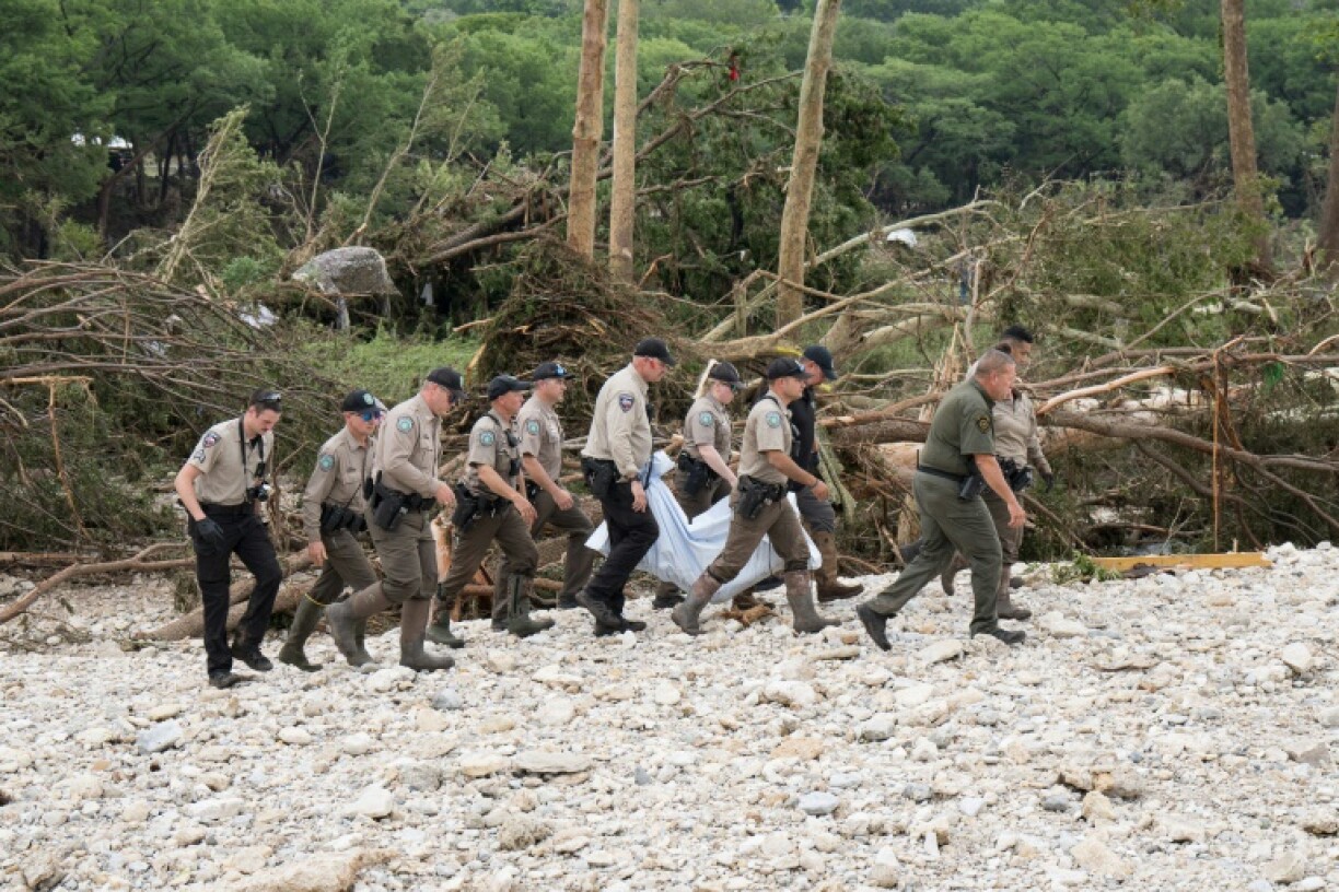 Texas Game Wardens and local law enforcement carry the body of a flood victim from the banks of the Guadalupe River during recovery operations near Hunt, Texas