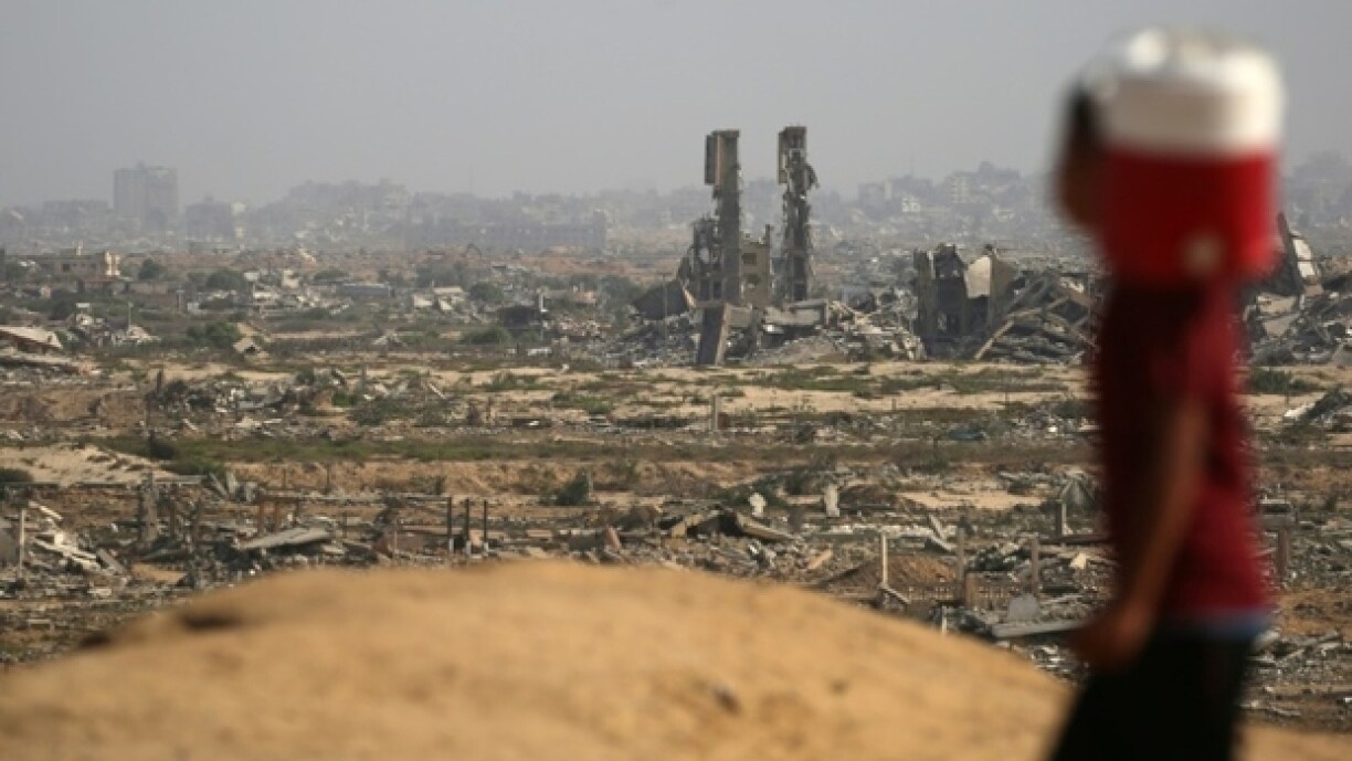 Un enfant palestinien portant un bidon d'eau passe devant des destructions sur une route côtière au nord-ouest du camp de Nousseirat, empruntée par des Palestiniens déplacés se rendant vers le sud de la bande de Gaza, le 4 octobre 2025