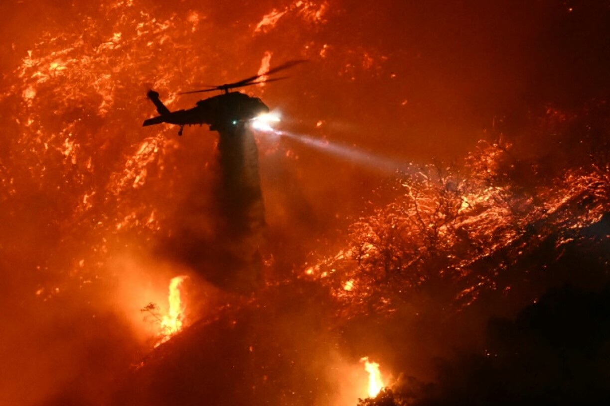 A helicopter drops water on the Palisades Fire as it grows near California's Mandeville Canyon and Encino neighborhoods on January 11, 2025