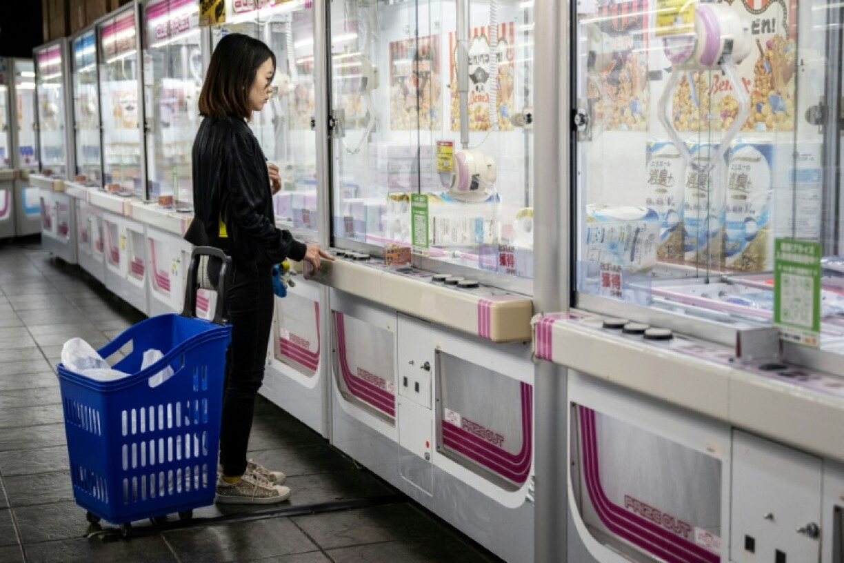 A patron stands with her shopping cart as she tries to win toilet paper at a claw machine game at the Benex amusement park in Kawasaki on October 5, 2026. As inflation weighs on Japanese households, huge arcades on the outskirts of major cities are installing claw machines filled with eggs, rice, laundry detergent and other necessities.