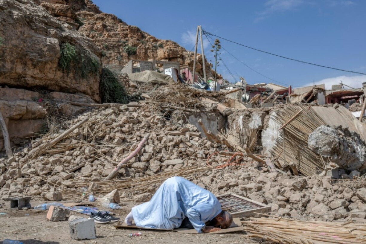 Photo prise le 12 septembre 2023 dans le village de Imi n'Talat, dans le centre du Maroc, montrant un homme priant devant des décombres de bâtiments après un puissant séisme