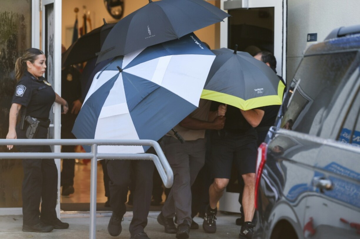 Flavio Bolsonaro and his family are shielded by umbrellas as they depart Opa Locka Executive Airport in Miami, Florida