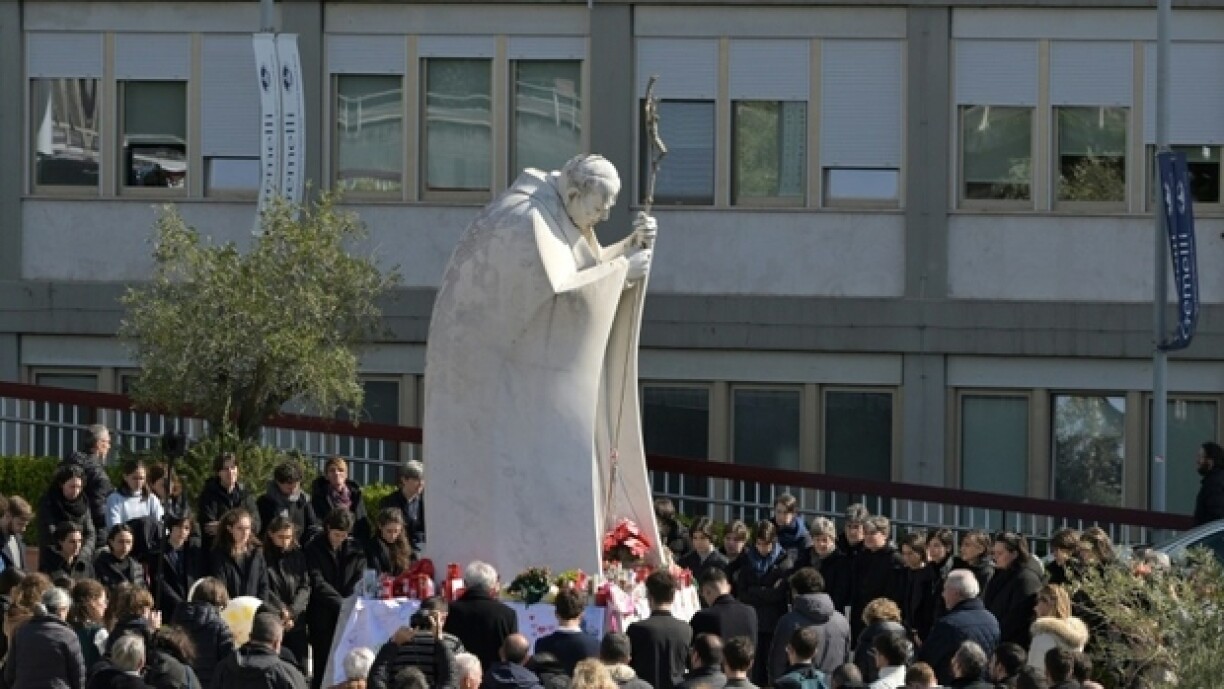 Des personnes prient autour de la statue de Jean-Paul II devant l'hôpital Gemelli à Rome où est hospitalisé le pape François, le 2 mars 2025