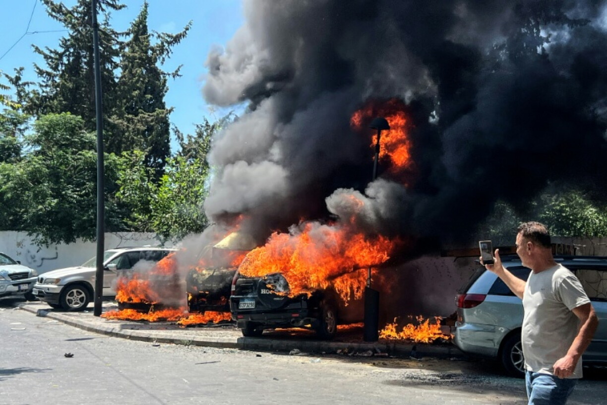 Un homme prend des photos de véhicules en feu après une frappe israélienne, le 10 juin 2026 à Saïda au Liban