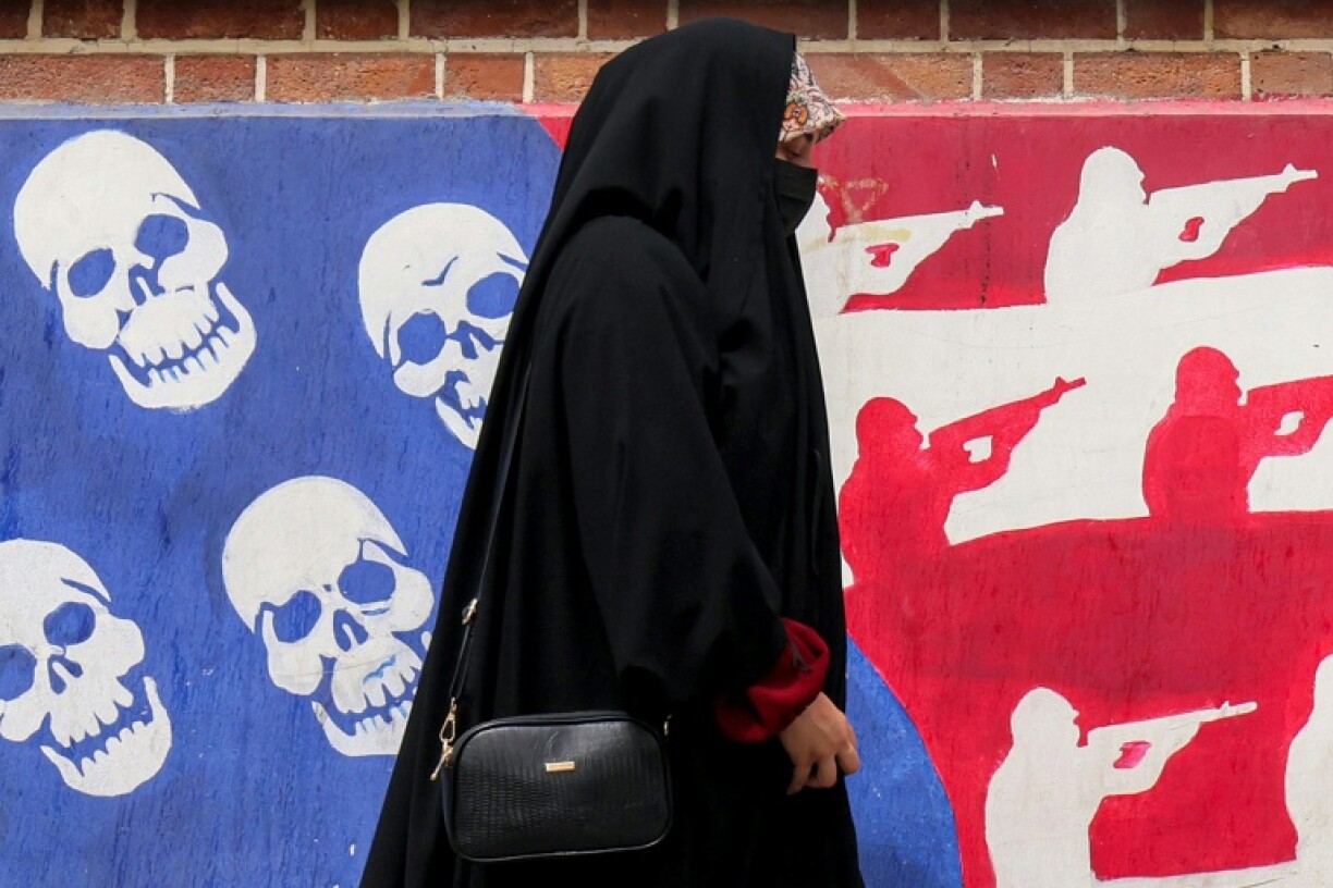 A woman walks past a mural on the walls of the former US embassy building in Tehran, known as the