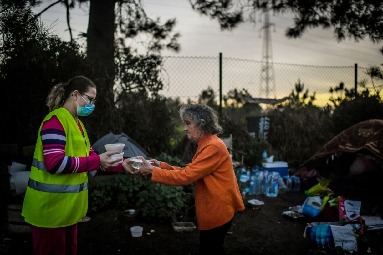 Une bénévole en train de distribuer de la nourriture à une personne âgée qui dort en tente à Sesimbra, près de Lisbonne.