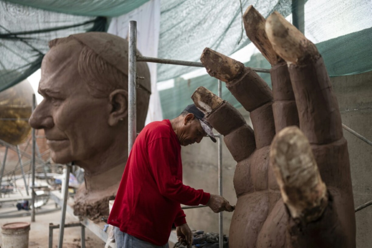 A craftsman adds clay to the fingers of the enormous hands of the sculpture