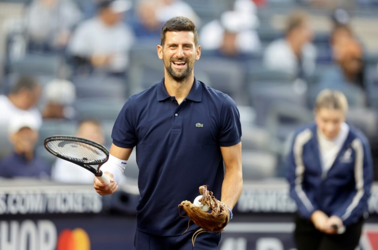 Tennis star Novak Djokovic carries his racquet to the mound before throwing the ceremonial first pitch at a New York Yankees baseball game