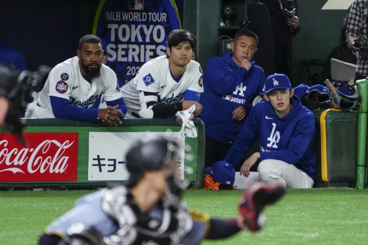 Los Angeles Dodgers' Shohei Ohtani (C) and Roki Sasaki (R) watch from the dugout during an exhibition baseball game against the Hanshin Tigers at the Tokyo Dome