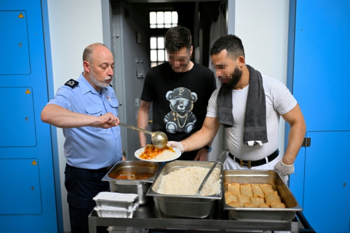 Un détenu, accompagné d'un agent pénitentiaire, sert un repas à un autre détenu, à la prison de Namur, le 23 juin 2026 en Belgique