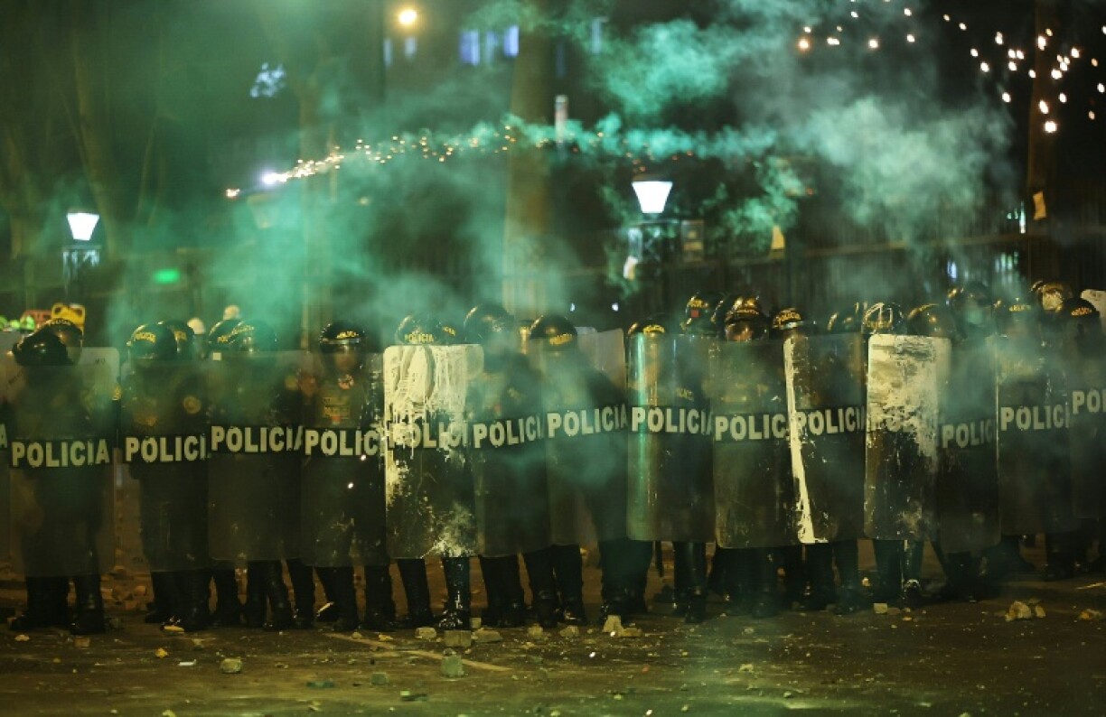 Anti-riot police officers take cover from fireworks as they clash with demonstrators during a protest against Peru's interim President Jose Jeri in Lima on October 15