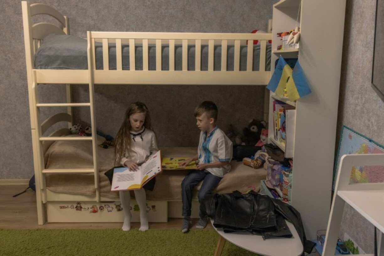 Nadiya Mikhailyuk lit un livre à côté de son frère Makar avant la rentrée des classes, le 1er septembre 2023 à Irpin, près de Kiev, en Ukraine