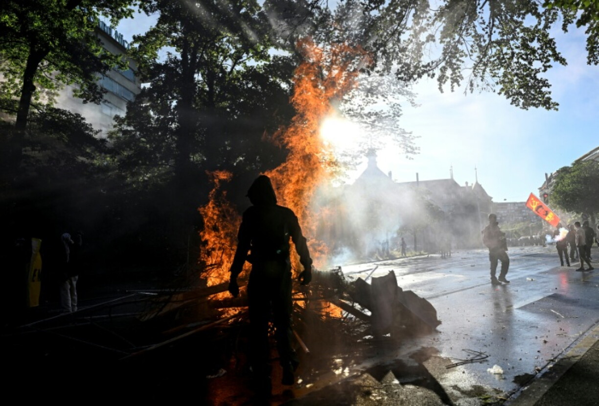 Manifestant devant une poubelle en feu lors d'une manifestation anti-G7 à Genève, le 14 juin 2026