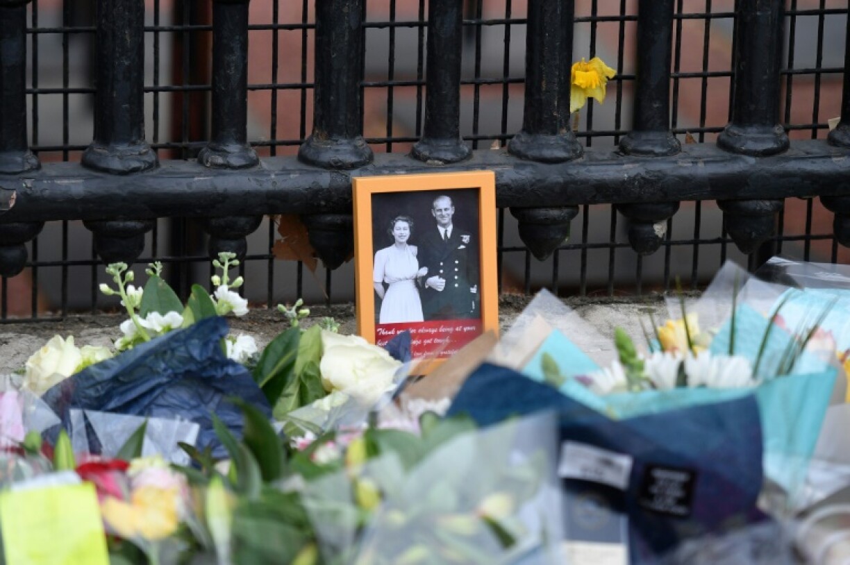 Un portrait de la reine Elzabeth II et du prince Philip au milieu des fleurs déposées devant les grilles du palais de Buckingham, le 9 avril 2021 à Londres