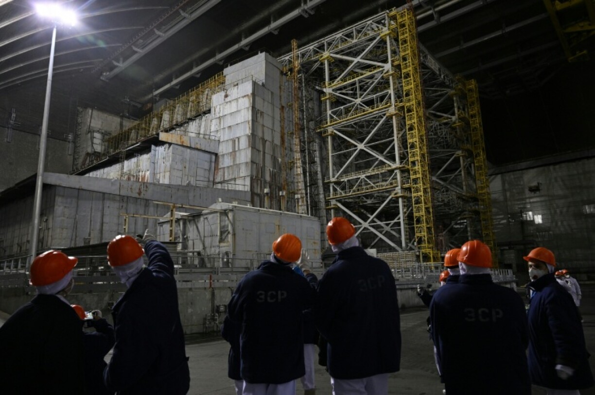 Des représentants de Greenpeace et des médias devant le sarcophage recouvrant le quatrième réacteur détruit sous l'enceinte de confinement, à la centrale nucléaire de Tchernobyl, le 9 avril 2026 en Ukraine