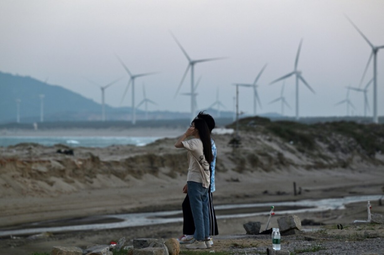 Des personnes sur une plage, devant des éoliennes sur l'île de Pingtan, le point de Chine continentale le plus proche de l'île principale de Taïwan, dans la province chinoise du Fujian (est), le 14 octobre 2024.