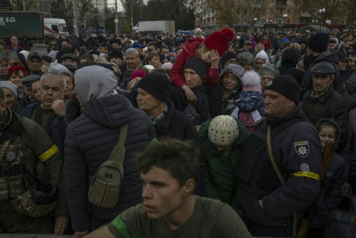 Un enfant sur les épaules d'un homme dans une foule attendant une distribution d'aide humanitaire à Kherson, le 19 novembre 2022